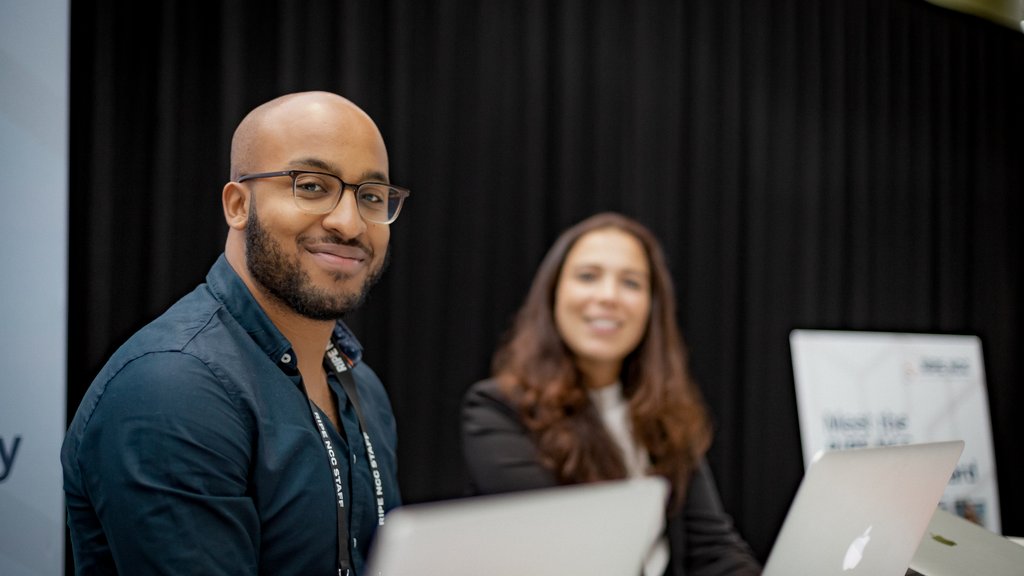 A man and woman sit at laptops smiling